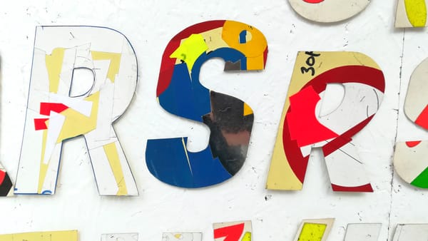 Letters cut out of cardboard and arranged in a line with a large 'R' and 'S' followed by a smaller 'R'.
