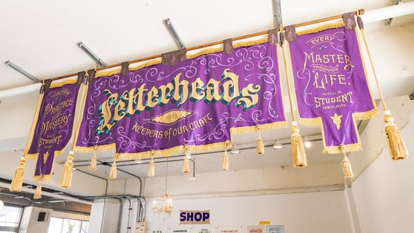 Horizontal purple banner in three parts with lettering, scrollwork, and decorative tassles.