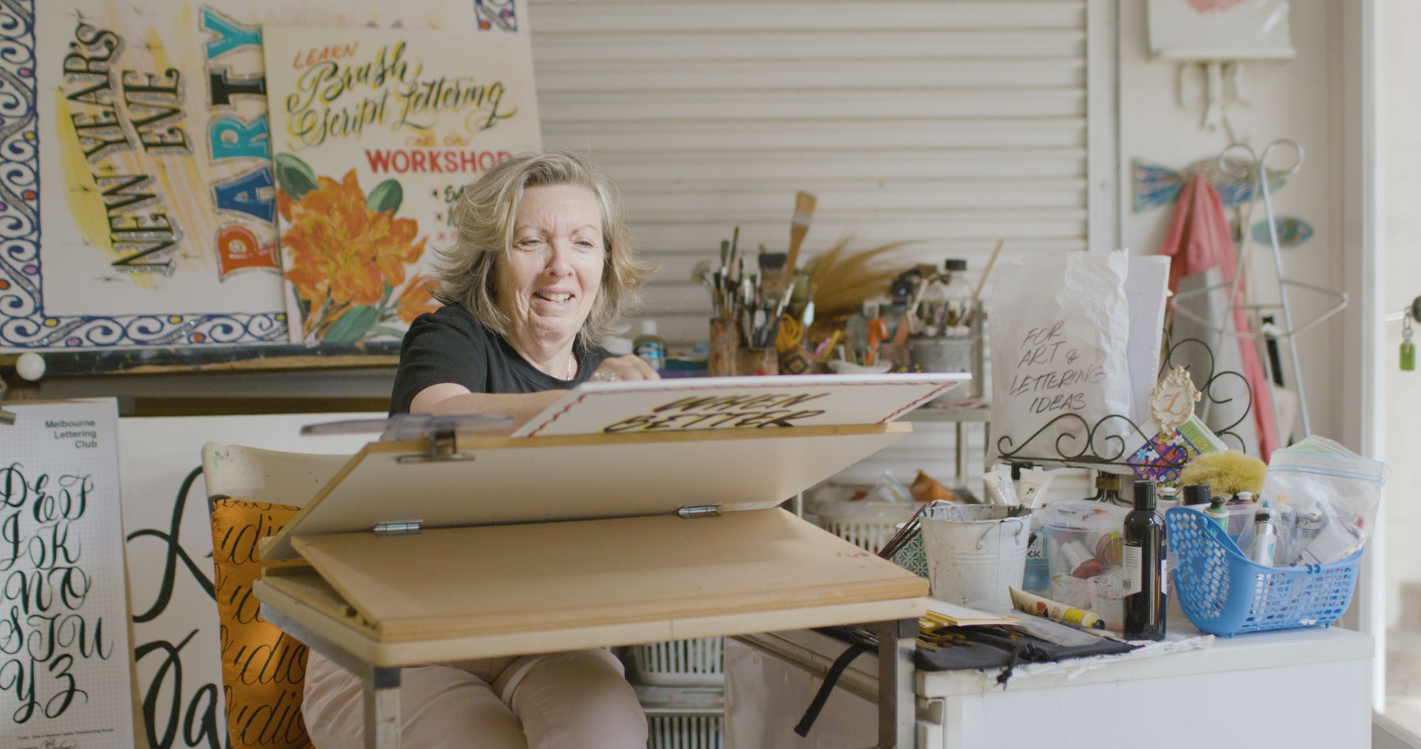 Woman smiling while working at an easel in an artists' studio.