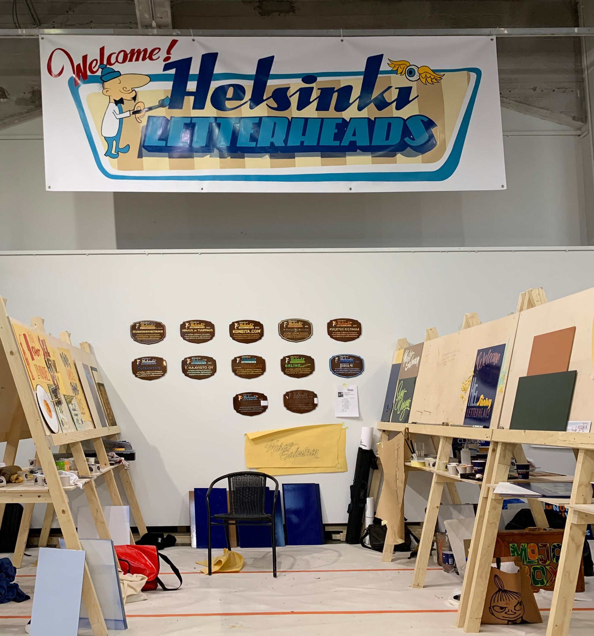 Array of easels and a hand-painted 'Welcome Helsinki Letterheads' sign.