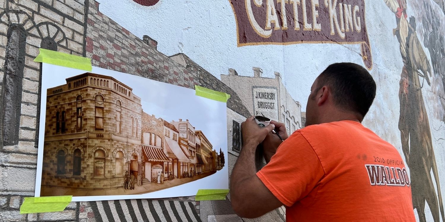 Man painting a mural with pictorial reference sheet.