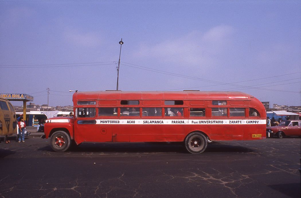 Red bus with stops lettered in black on a horizontal white band.