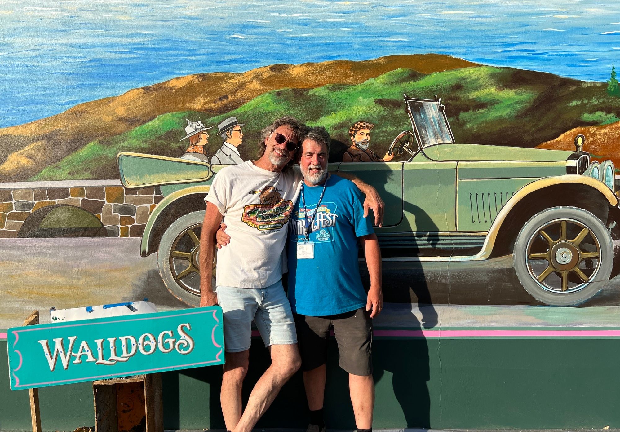 Two men standing in front of a painted car on a wall.