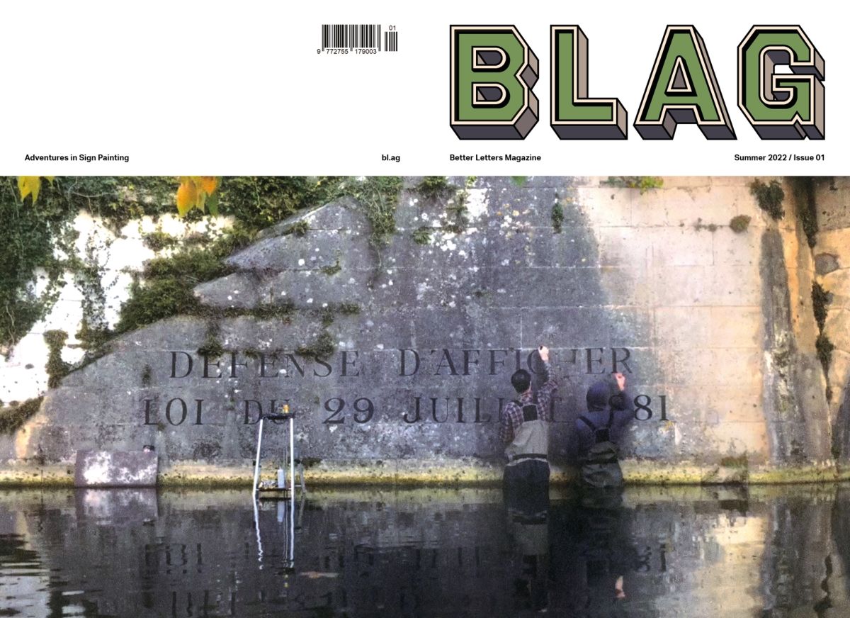 Magazine cover showing two sign painters standing in a river, working on a wall.