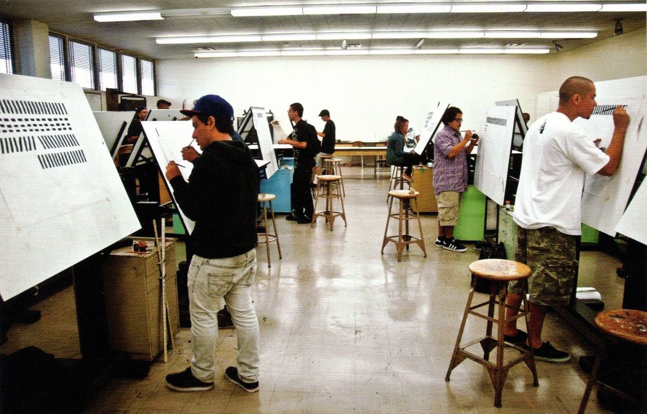 Students painting lettering practise strokes at upright easels.