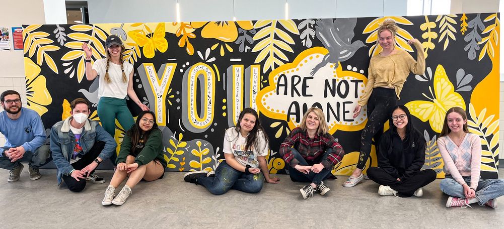 Artists and student in front of a painted mural that reads "you are not alone".