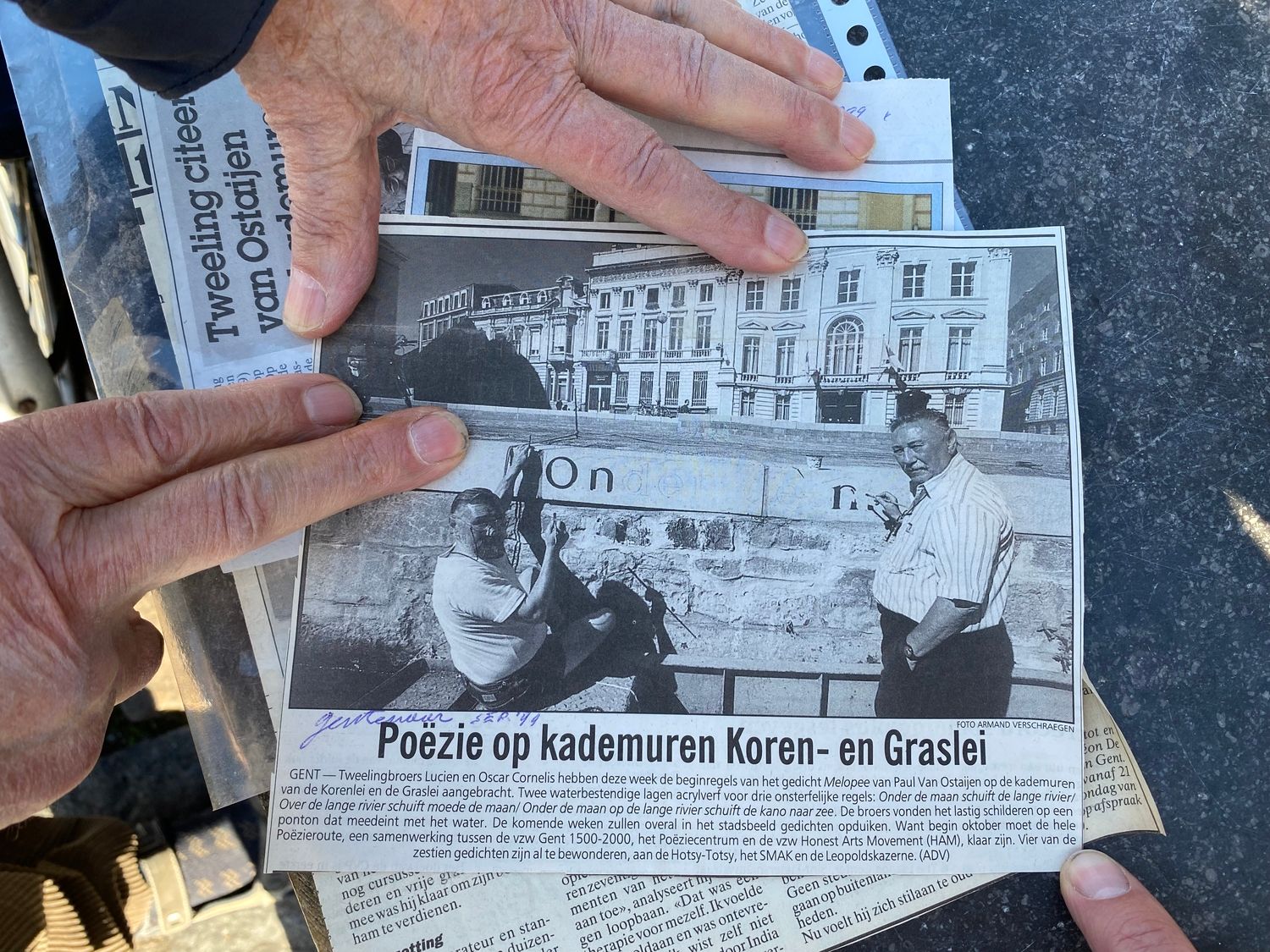 Newspaper clipping showing two men posing in front of a wall they are painting letters onto.