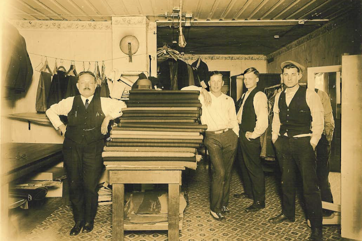 Archival photo of men posing with fabrics in a taliors shop.