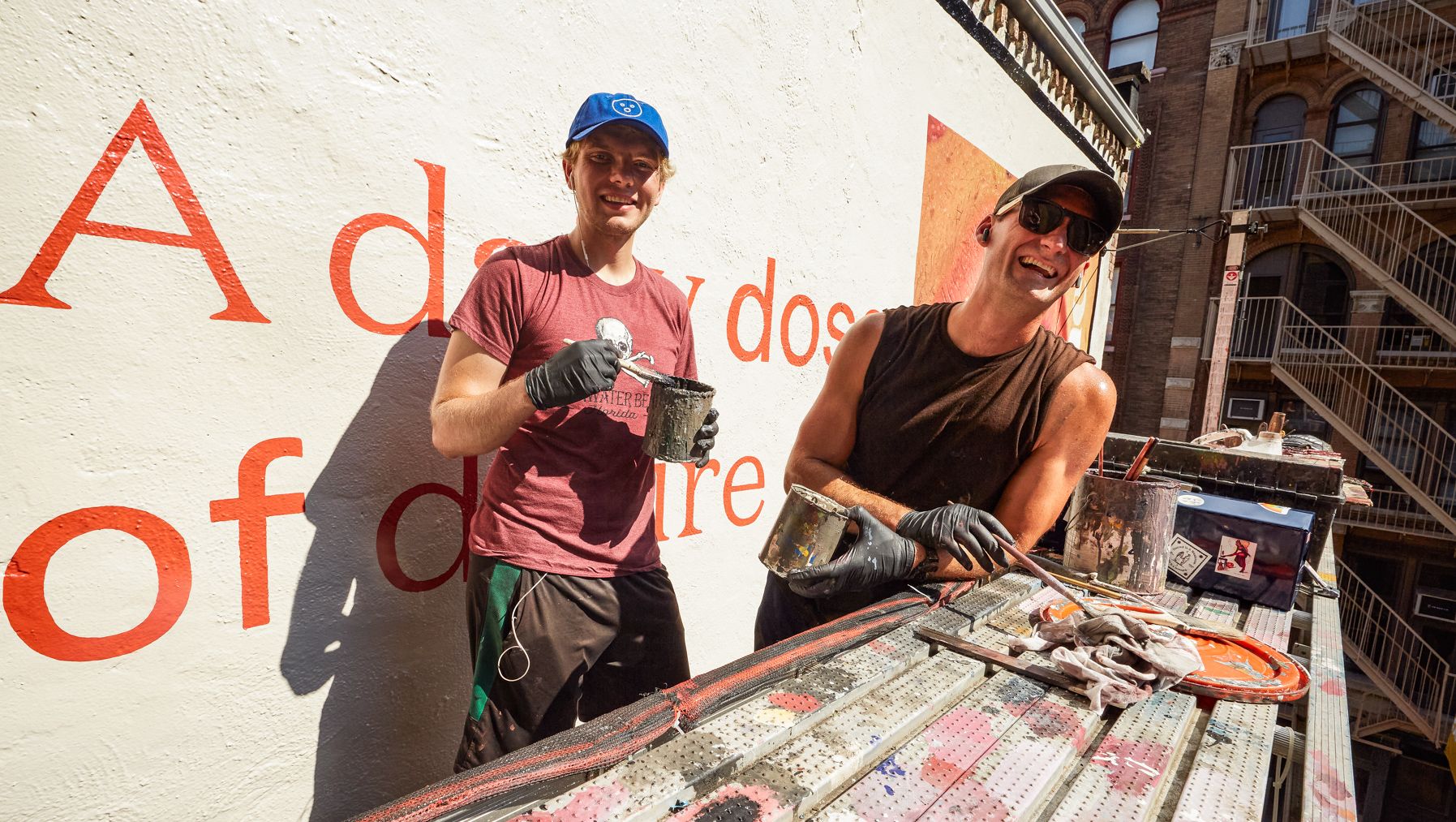 Two painters in front of a wall on which they are painting red letters.