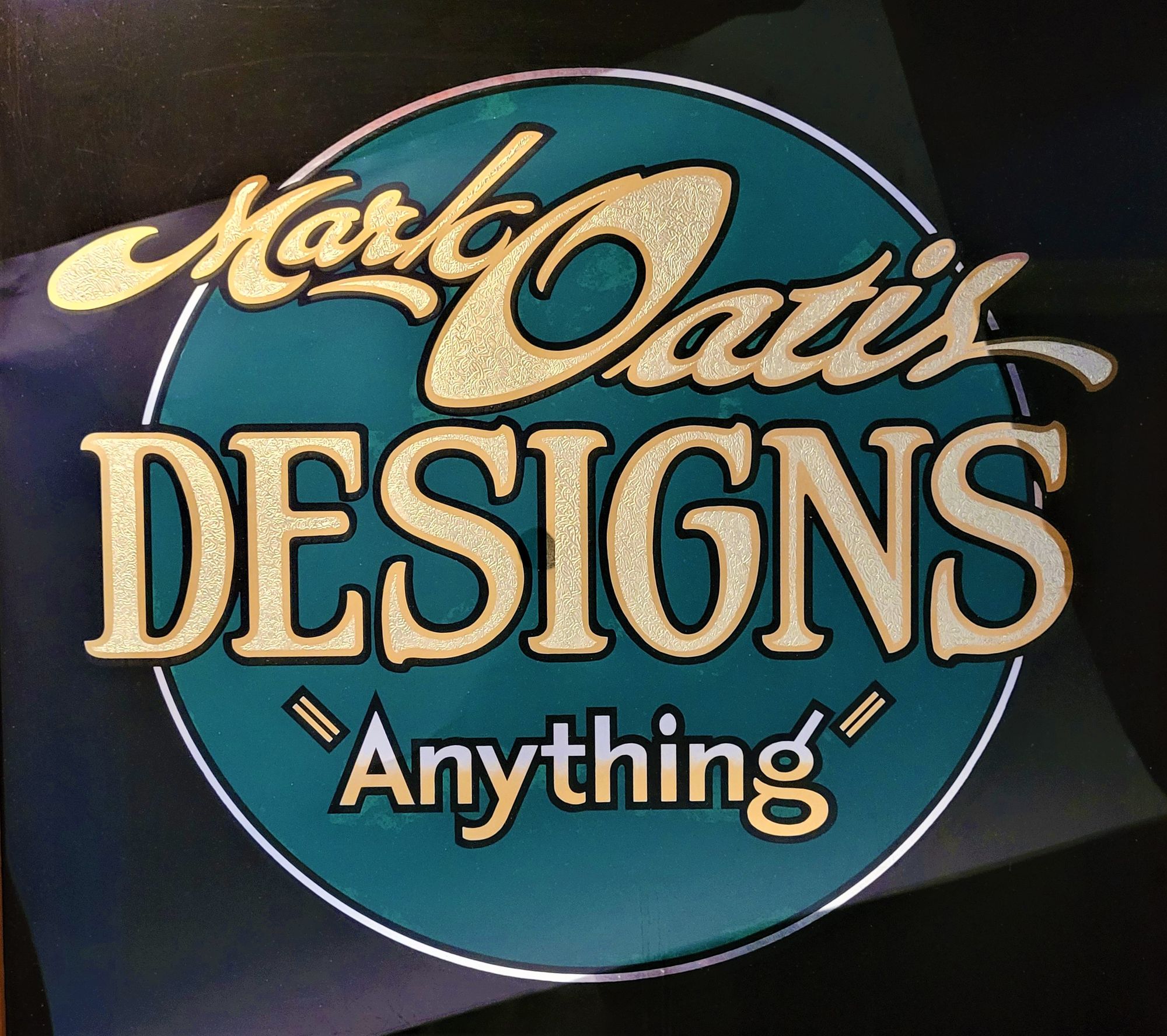 Hand-lettered and gilded glass panel reading 'Mark Oatis Designs "Anything"'.