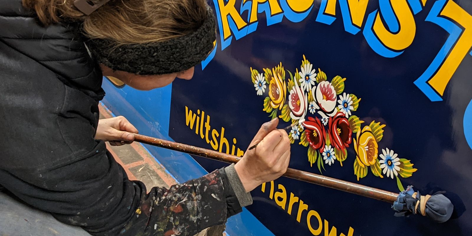 Signwriter resting their hand on a mahl stick while painting an arrangement of red, yellow, and white roses.