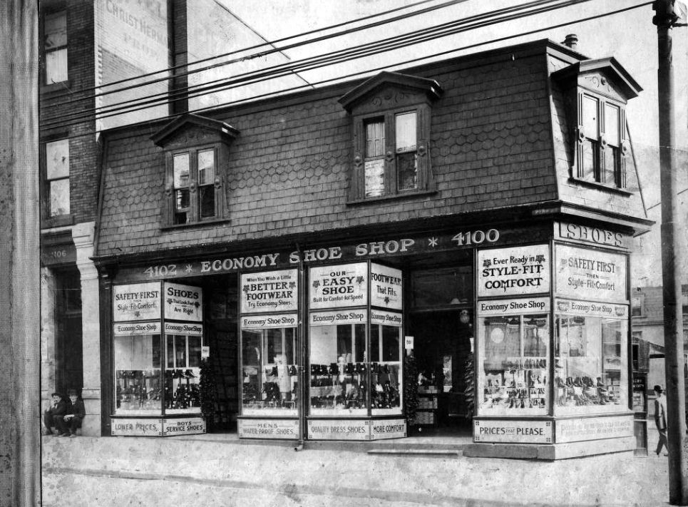 Two-story building with the ground floor housing a shoe shop and it's myriad pieces of window signage.