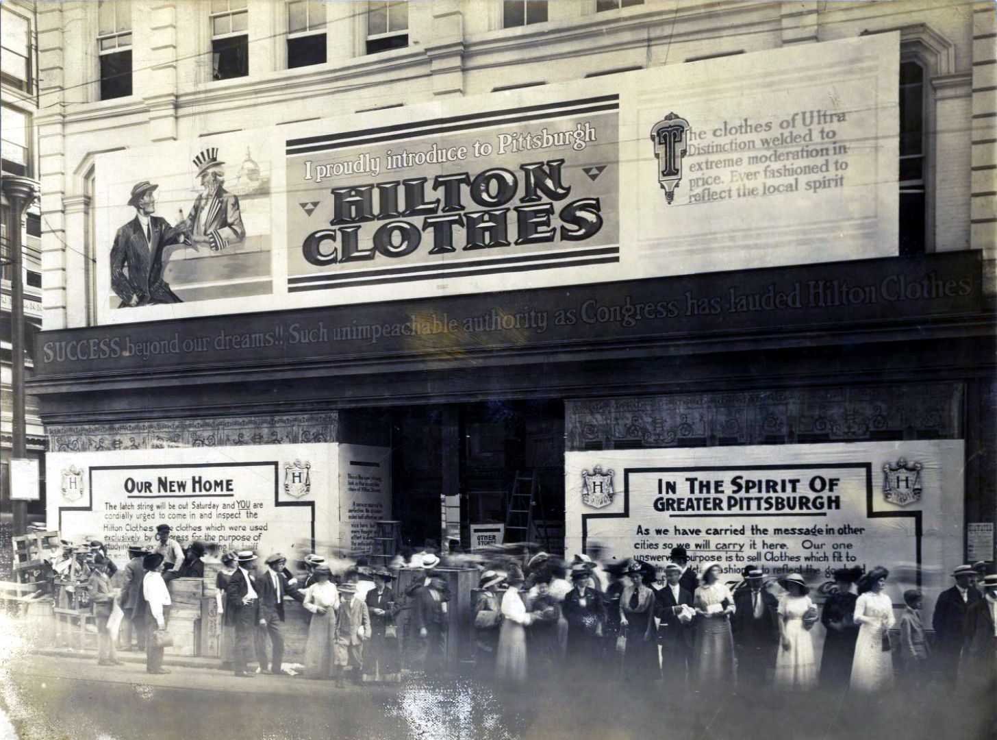 Large retail premises on a corner with huge pieces of signage adorning the building, and a crowd of people in period dress standing waiting outside.