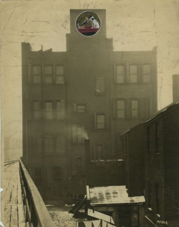 Photo of a tall industrial building with a hand-drawn circle at the top containing a dog listening to a gramophone.