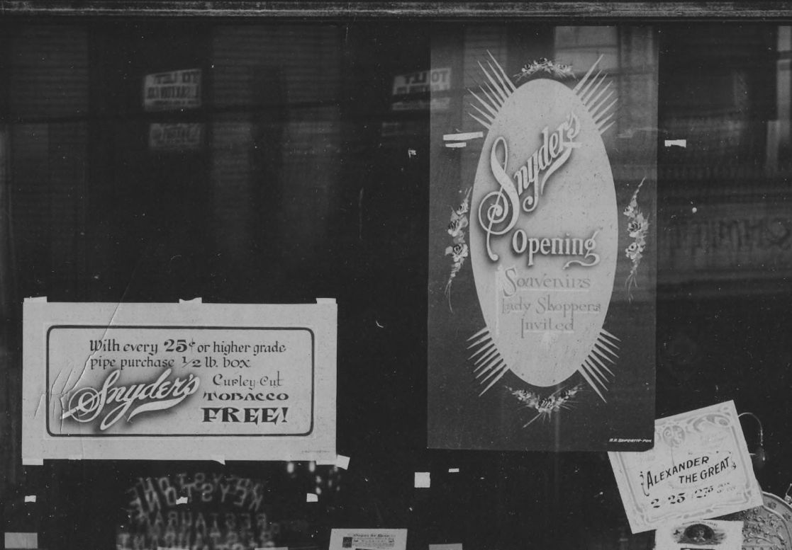 Hand-painted showcards taped to the inside of a window, advertising offerings from the cigar retailer.