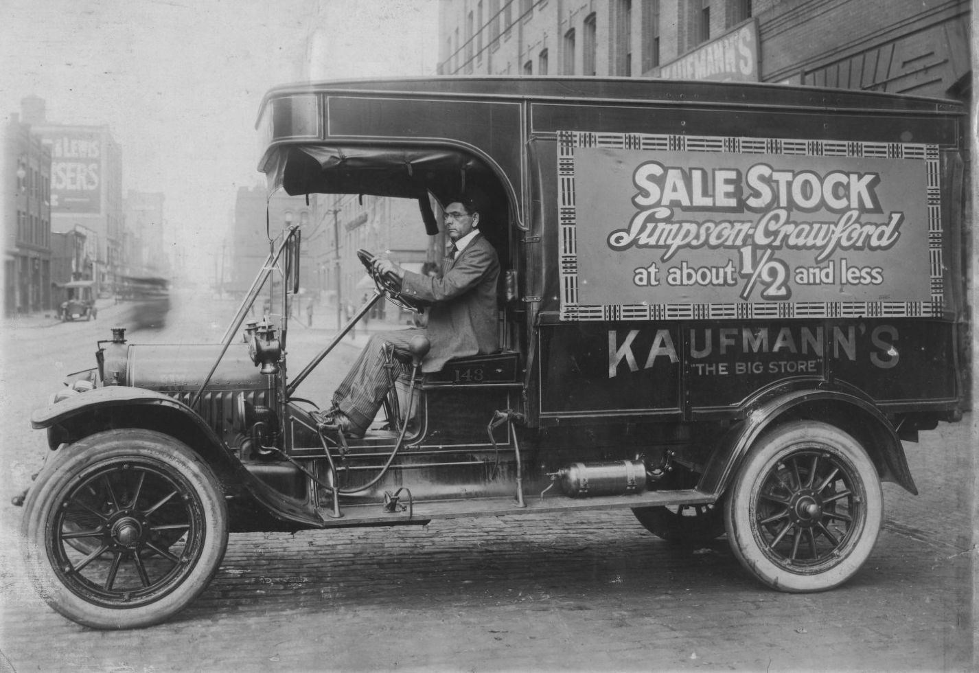 Man sat in the driver's seat of a vintage commercial vehicle adorned with temporary sale signage.