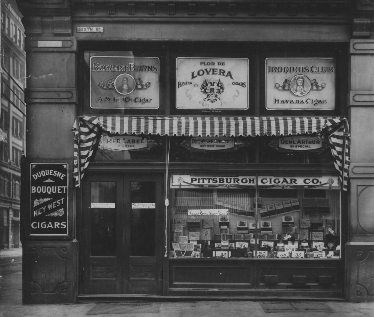 Archival image of a cigar and tobacco shop with various signage elements and a window display visible.