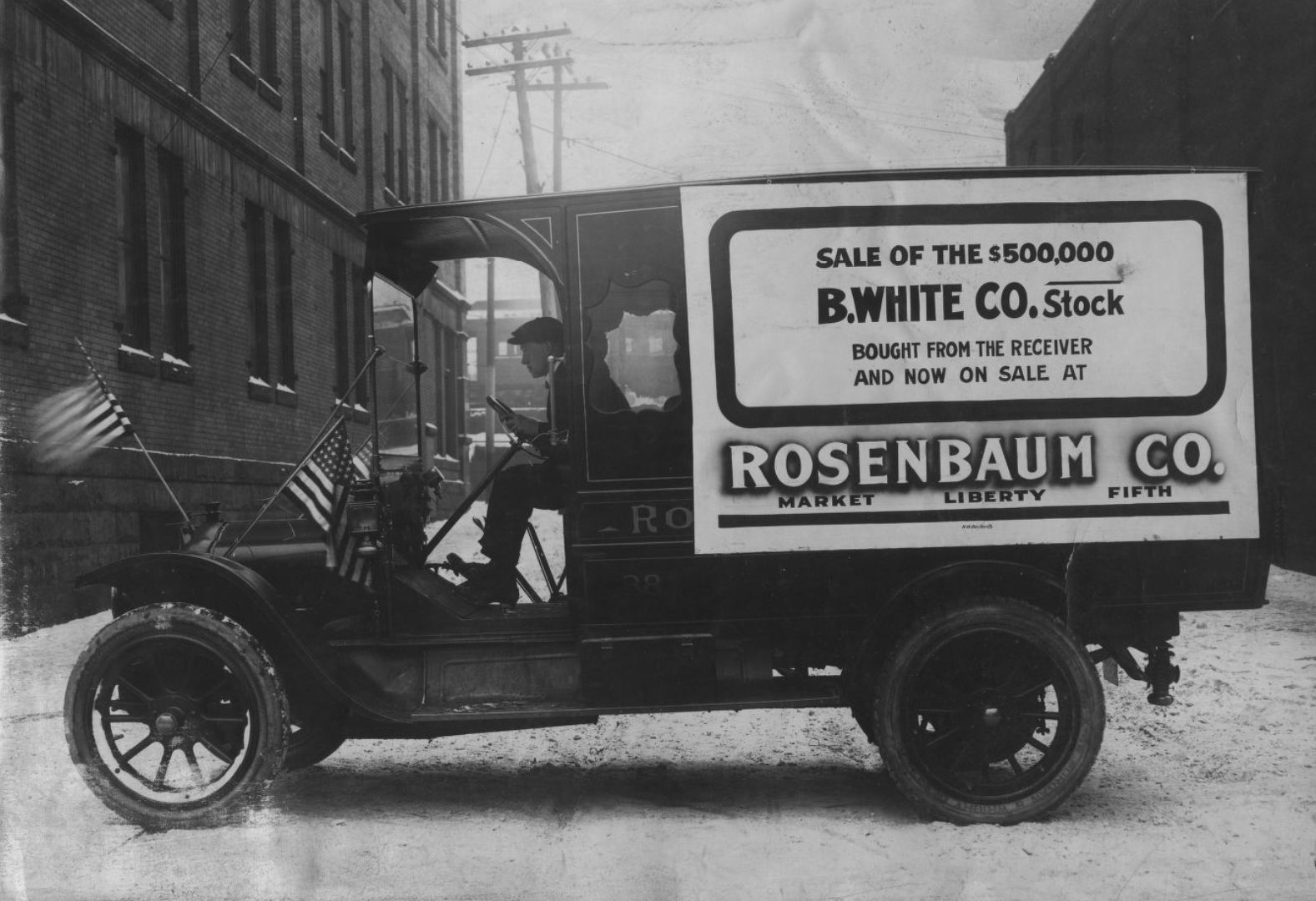 Man sat in the driver's seat of a vintage commercial vehicle adorned with temporary sale signage.