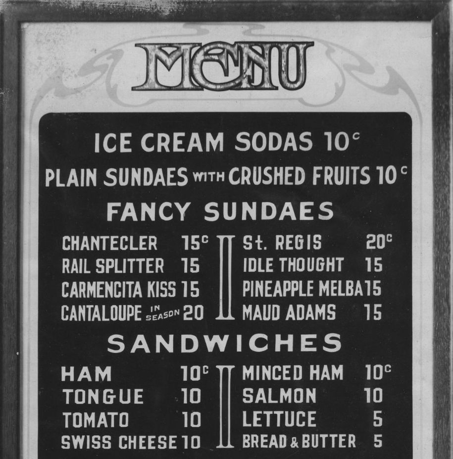 The top of a menu board with the word "Menu" in overlapping Art Nouveau lettering and items including sundaes and sandwiches below that.