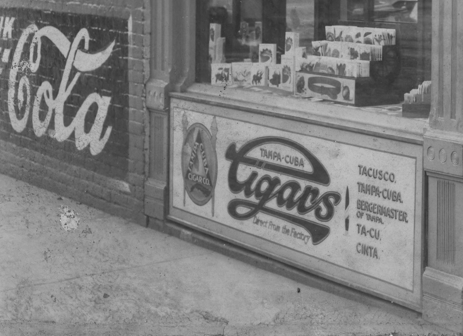 Window display with framed glass signage underneath and a painted wall sign to the side.