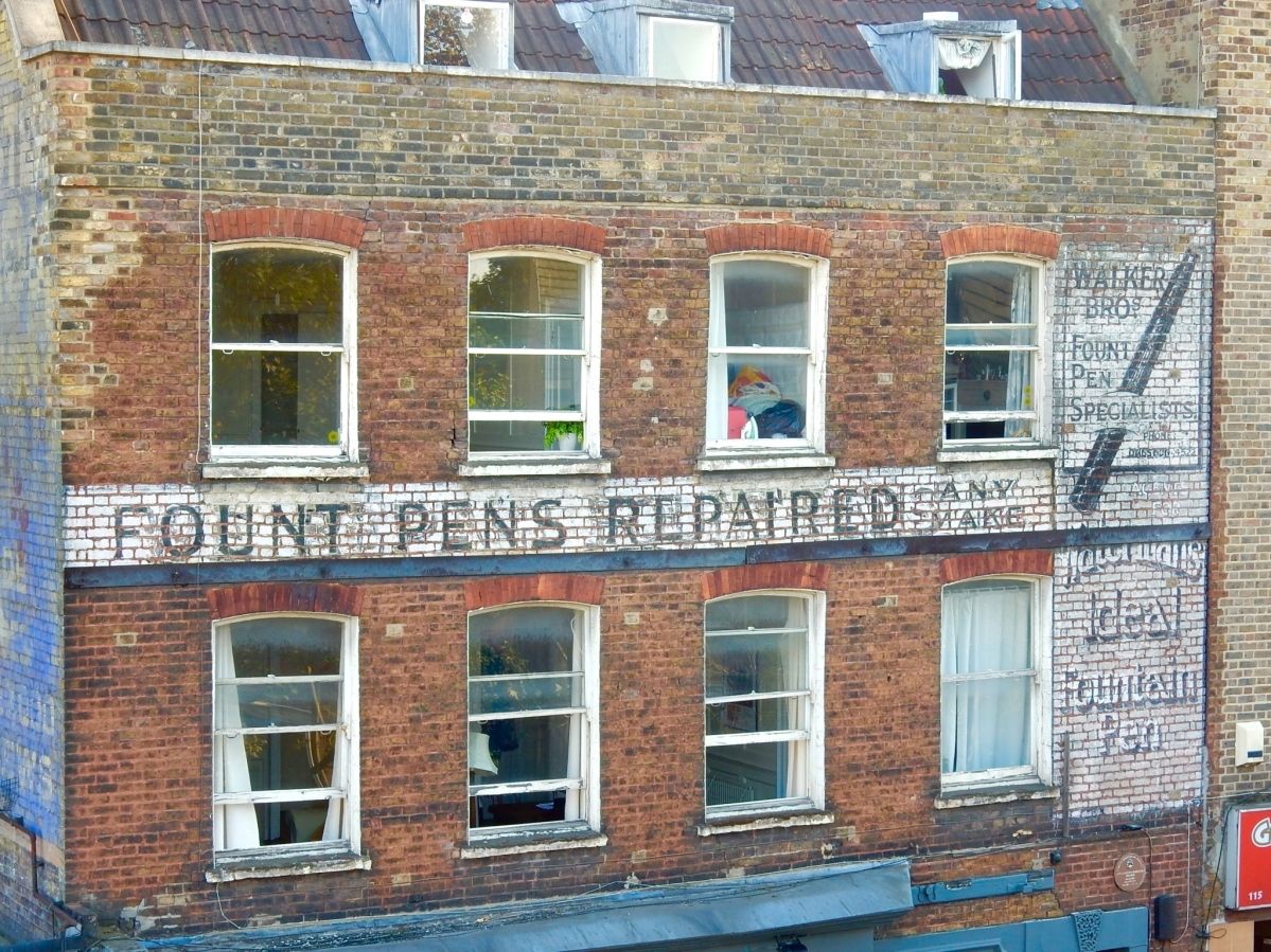 Fading painted sign on brick building advertising fount pens and their repair.