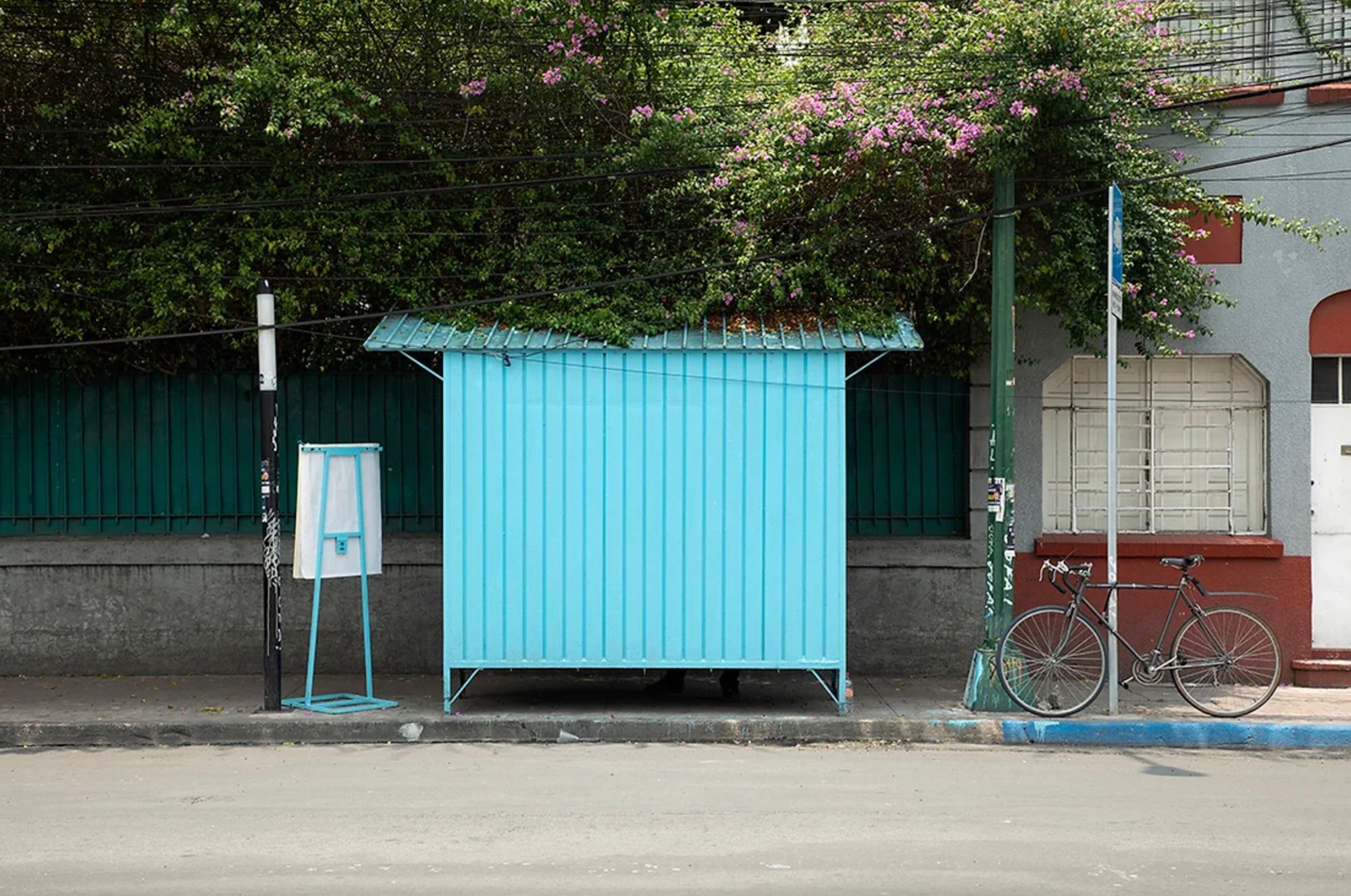 Simple street seen with an unidentified stand, bicycle, trees, lamppost and building.