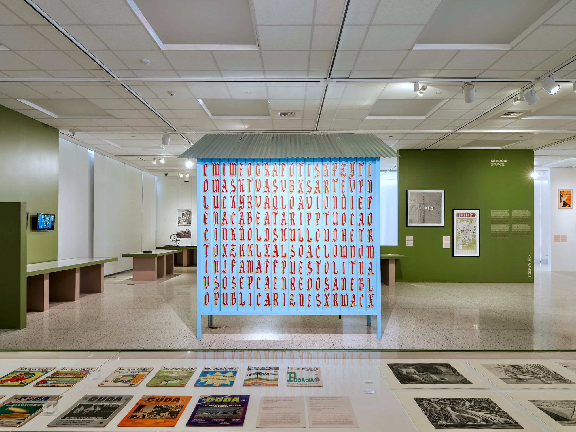 Gallery setting with graphic design work in cabinets in the foreground, and a wooden stall with hand-painted letters in the middle.