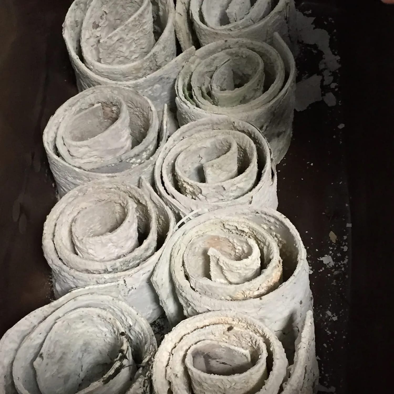 View of the tops of rolled sheets of leads, with a rough plaster-like appearance, and forming spiral shapes.