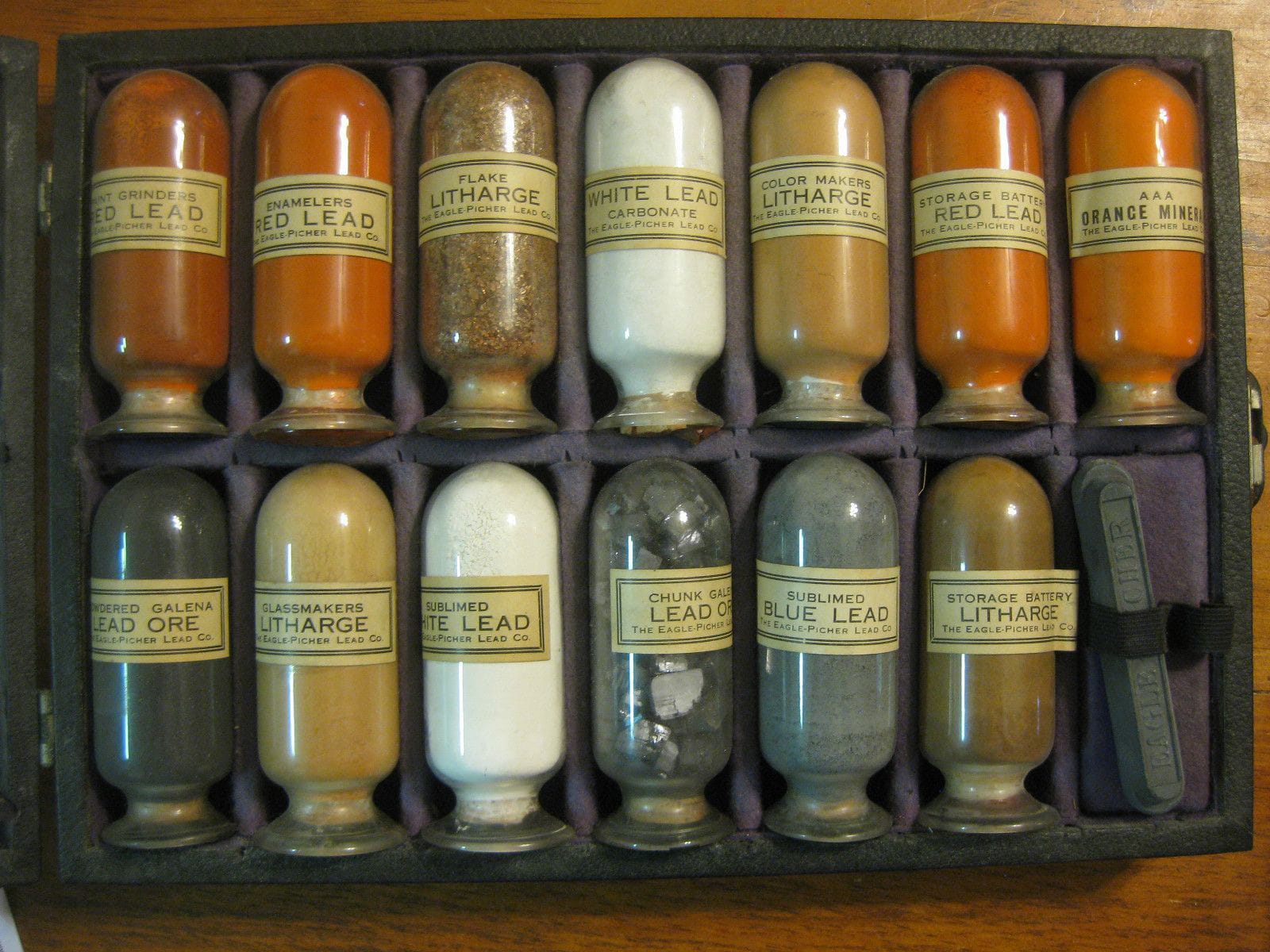 Presentation case with glass containers holding powdered substances in various colours, and labelled as different types of lead.