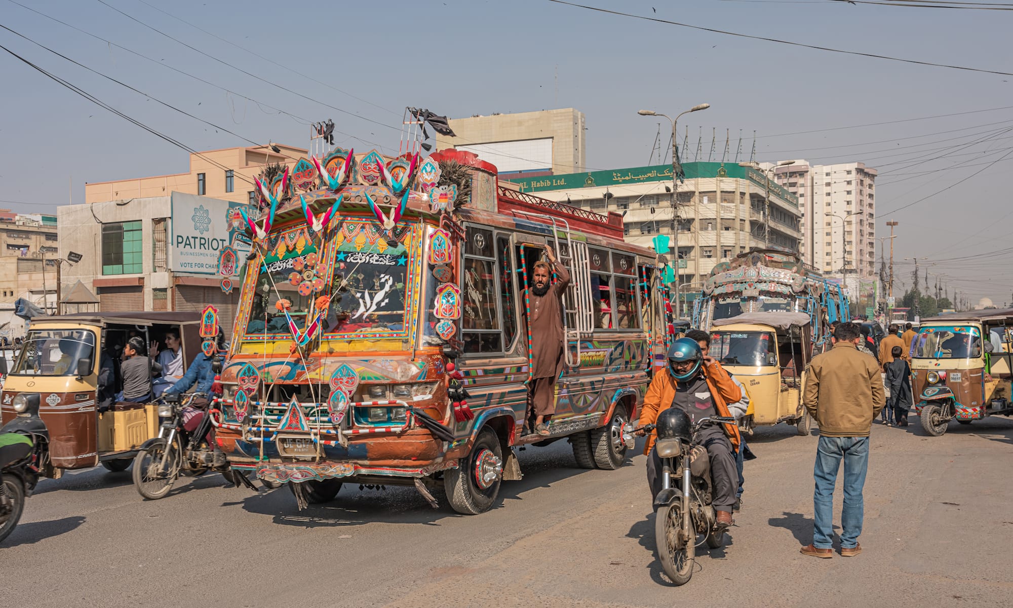 Busy street scene with a decorated bus amongst other traffic including motorbikes and tuktuks.