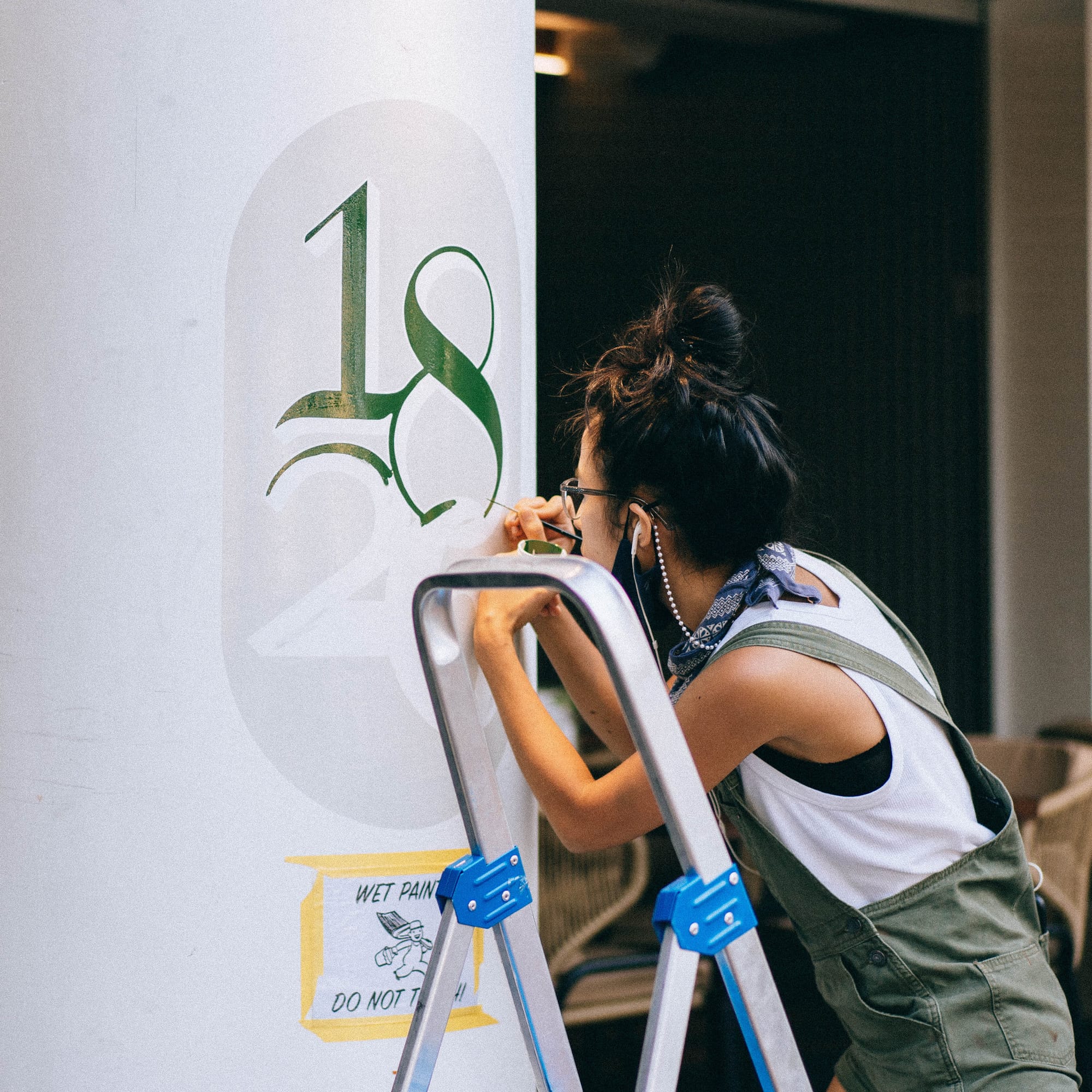 Woman painted numbers in green on a white pillar.