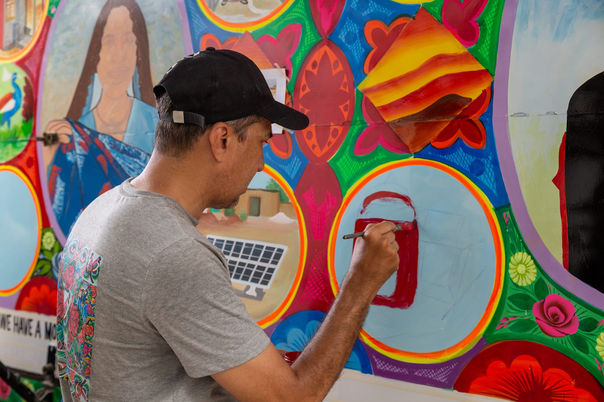 Man painting a picture within a wider brightly coloured composition on the side of a truck.