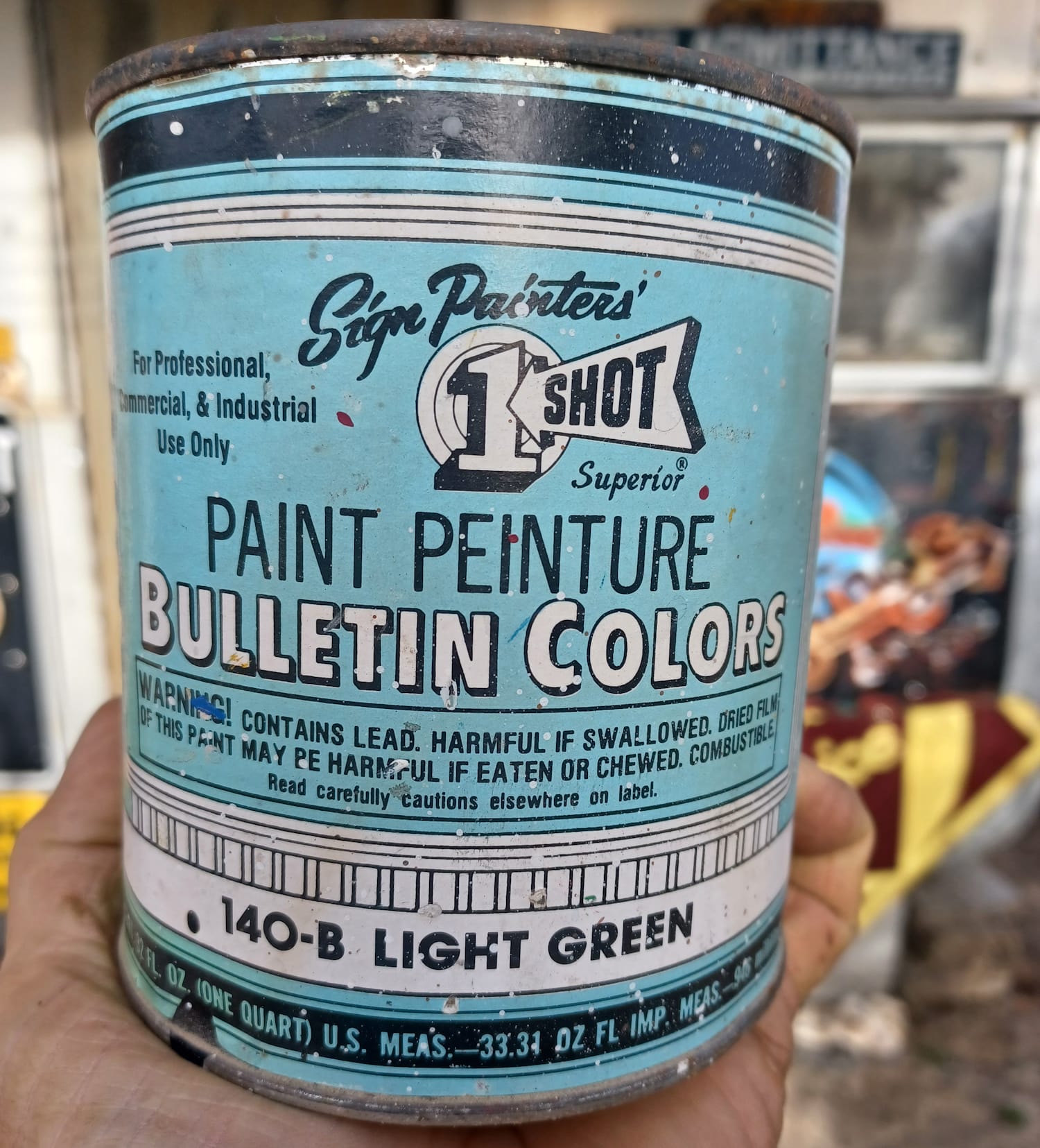 Hand holding a tin of paint with a label in black and white on light blue.