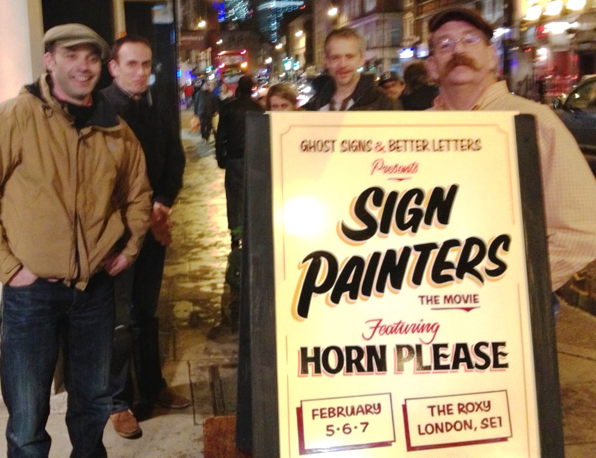 Group of men at night on a London street, with a hand-painted A-Board in front of them advertising a film screening.