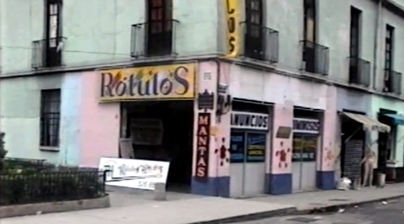 Street corner with a shop adorned with various pieces of signage, including the main fascia sign that reads "Rótulos".