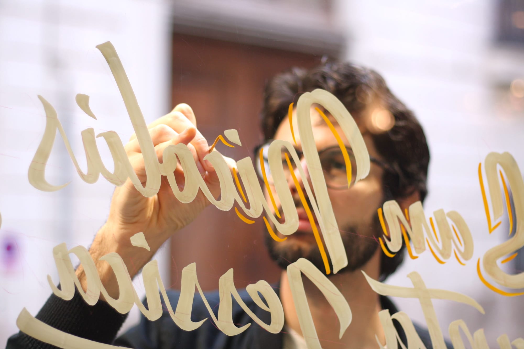 View through glass of a man applying a yellow offset shade to some lettering on the window.