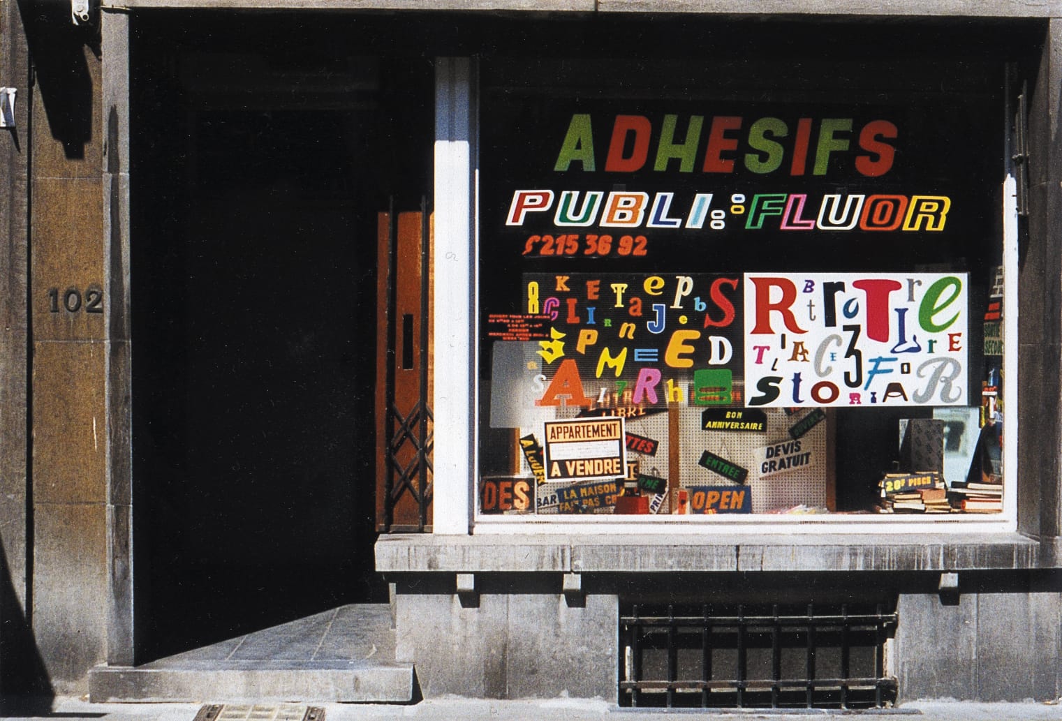 Shop front with a window display dominated by various colourful letters. Some make out the shop name and phone number, while others are in rectangular arrays to show off various styles and colours.