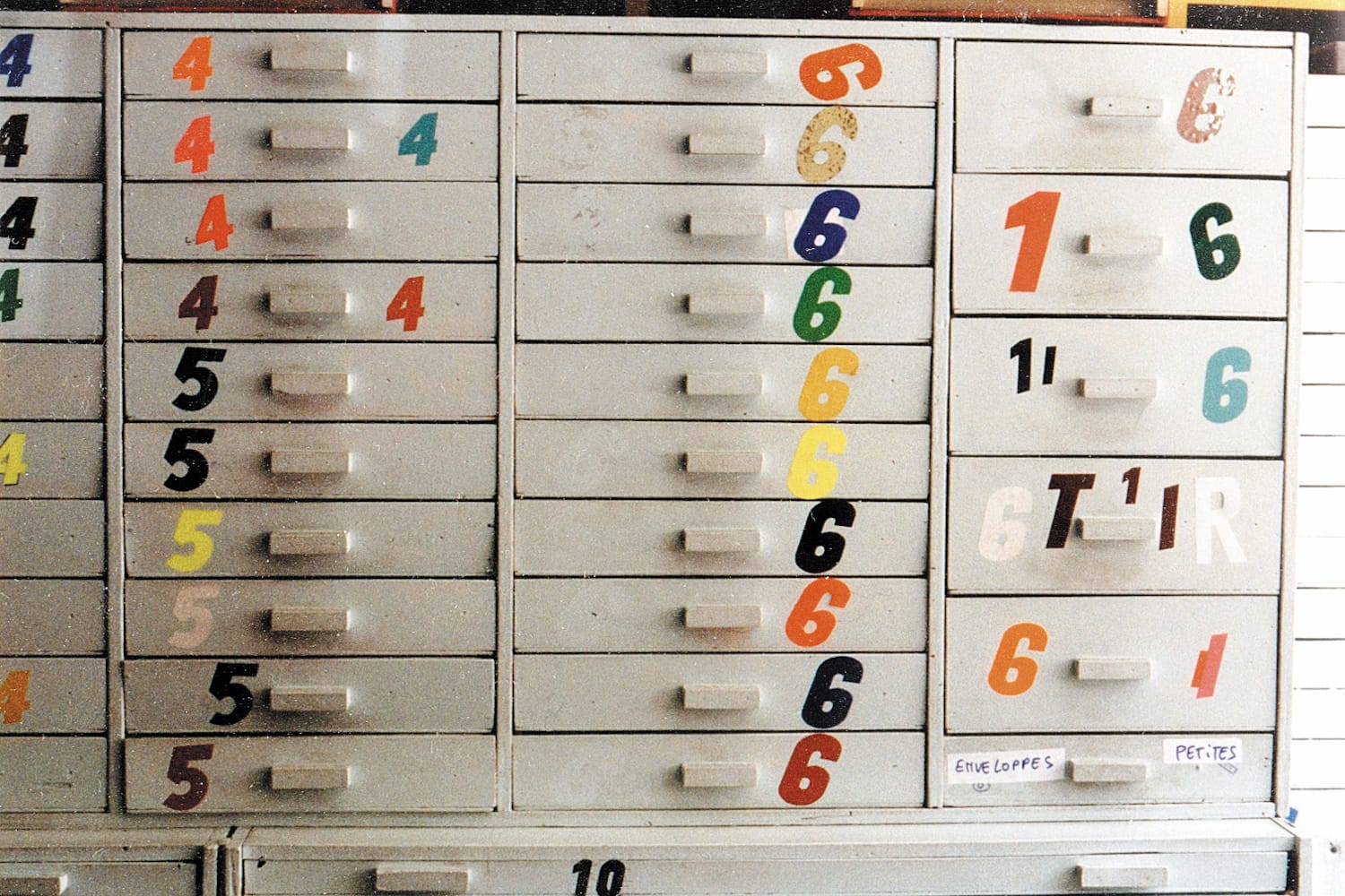 Array of grey drawers, each of which has a coloured number stuck to it beside the handle.