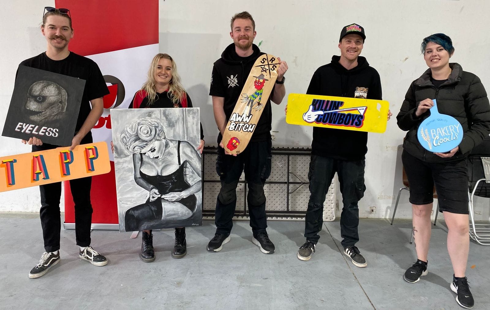 Five people standing in a line proudly holding various pieces of hand-painted artwork and lettering in front of them.