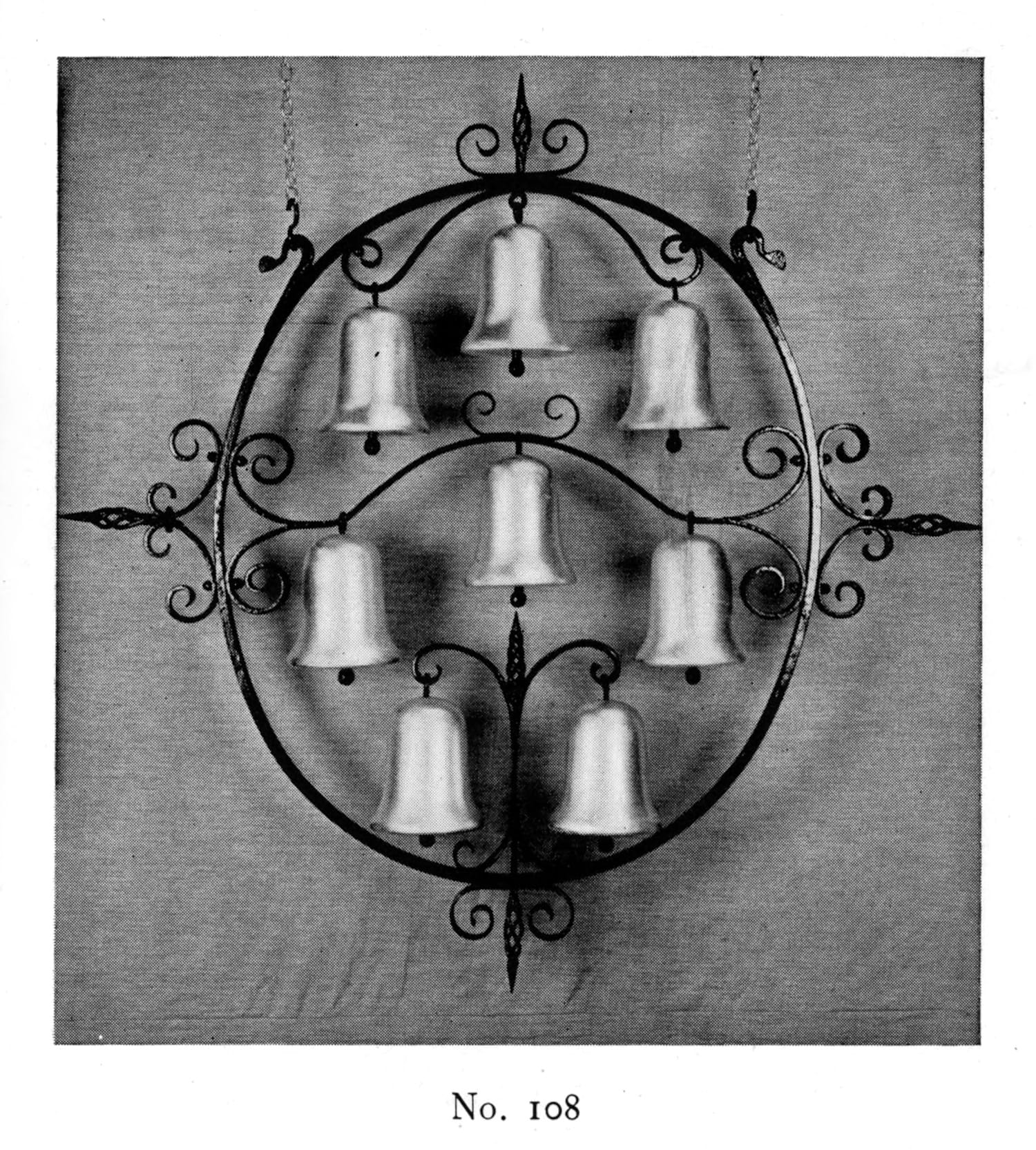 Hanging sign made of a decorative wrought iron frame with eight bells hanging from it. The bending of elements of the frame means that one bell sits in the middle, with the seven others forming an upright oval around it. 