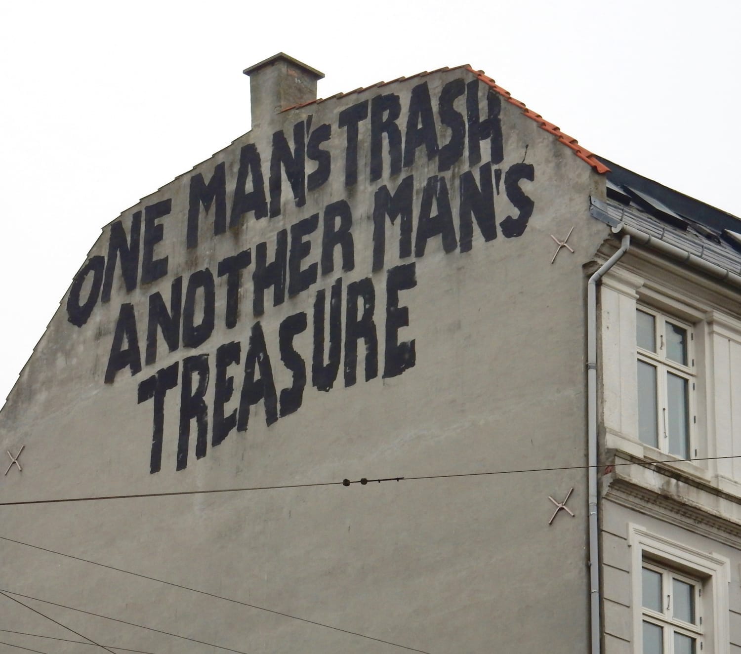 Top of a gable end wall with large black letters painted on it that say "One man's trash, another man's treasure".