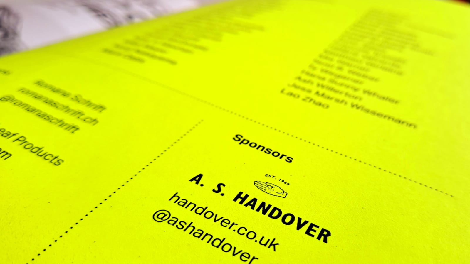 Close-up photo of the inside cover of a magazine in fluorescent yellow. Most of it is out of focus while visible in the foreground is the word "Sponsors" and then the A.S. Handover logo, website, and social media profile.