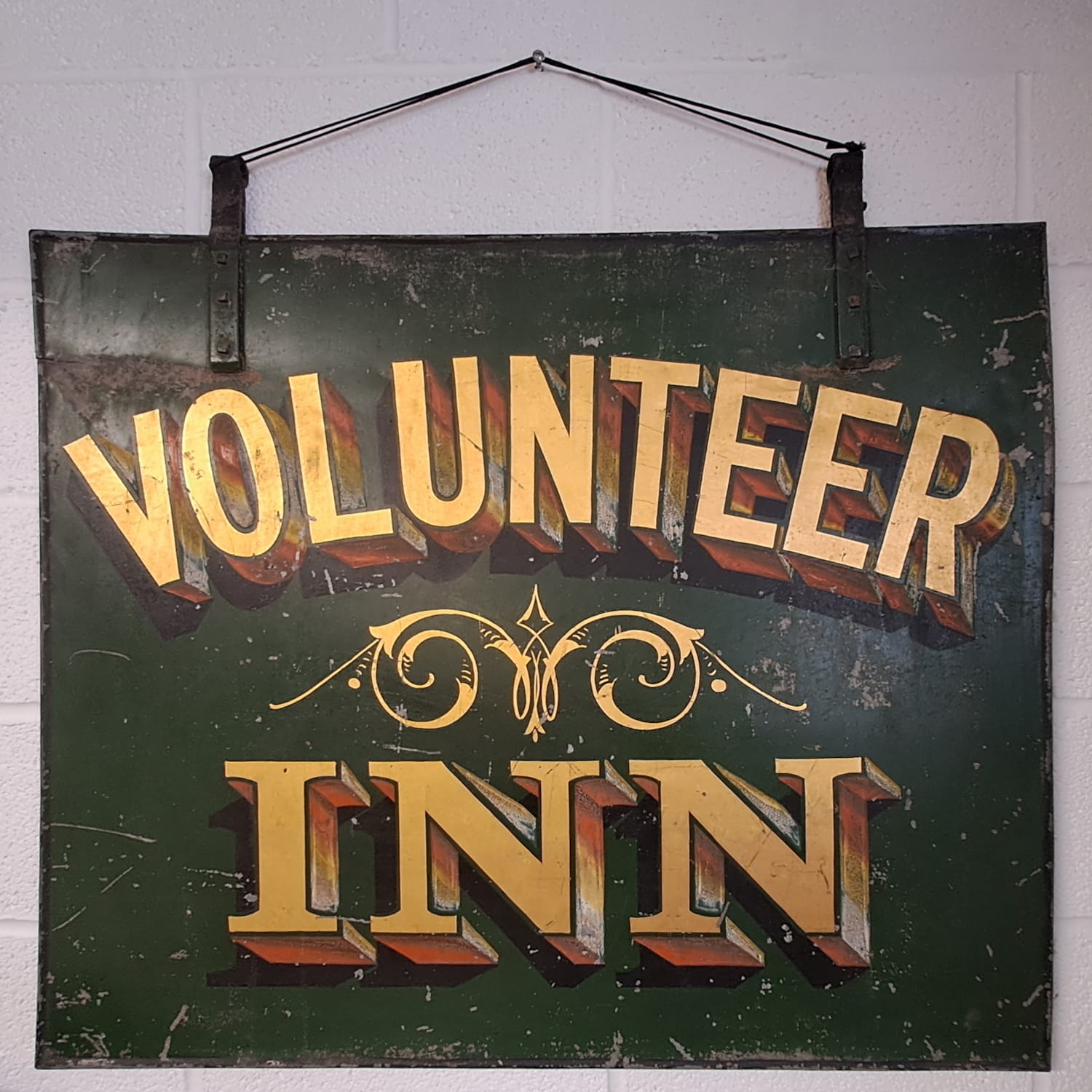 Old hanging sign on a wall with gilded and painted lettering that says "Volunteer Inn" with some scrollwork between the two words.