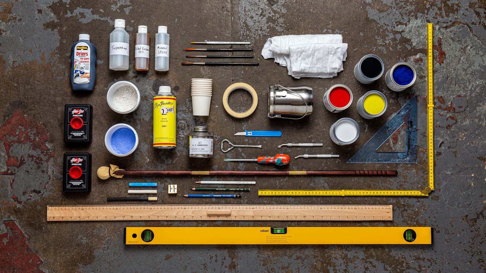 Paints, brushes, and other sign painting tools and materials arranged neatly on a surface and photographed from above.