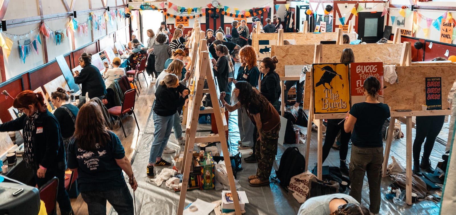 Photo from an elevated position looking slightly down on a community hall that's filled with A-frame easels and people painting all sorts of signs and lettering on them.