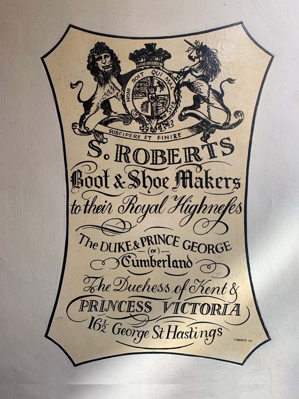 The sign is set on panel in the shape of a cow hide with a coat of arms at the top and period lettering that reads: "S. Roberts, Boot & Shoe Makers to their Royal Highneses The Duke & Prince George of Cumberland, The Duches of Kent & Princess Victoria, 16 1/2 George St Hastings. T. Noakes, 2009."