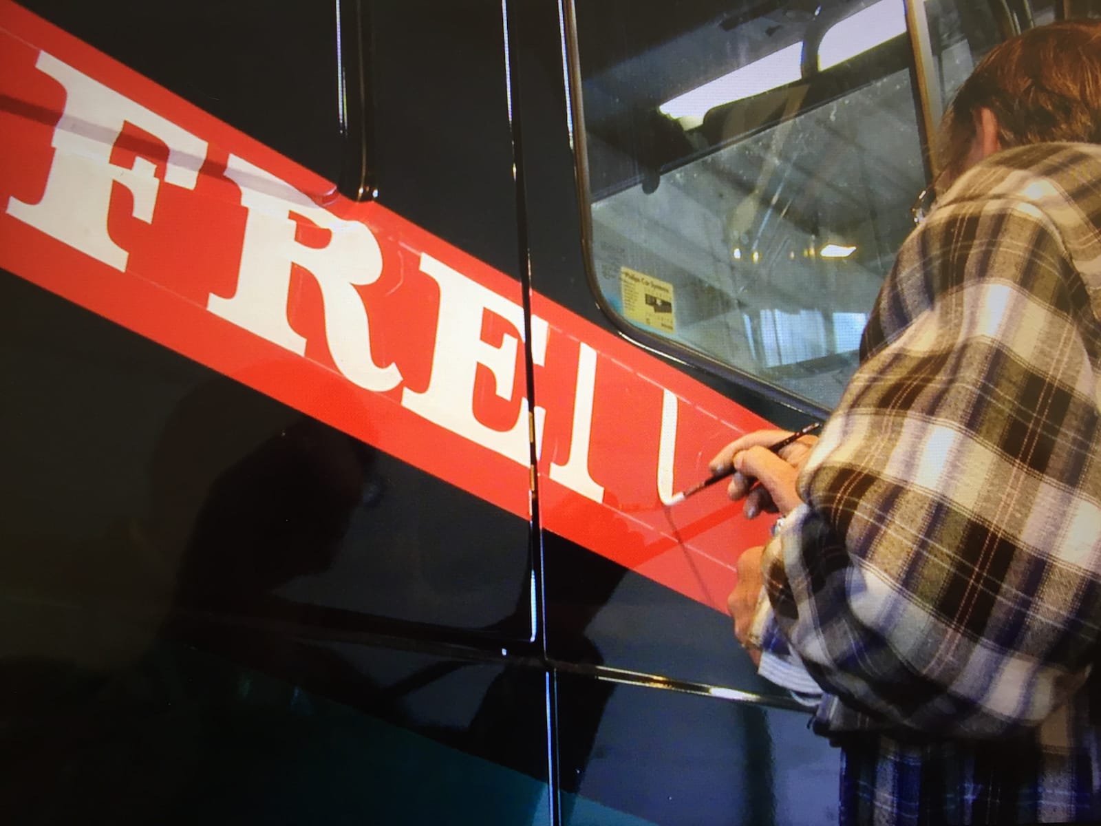 View from below a man painting white lettering onto a red background.