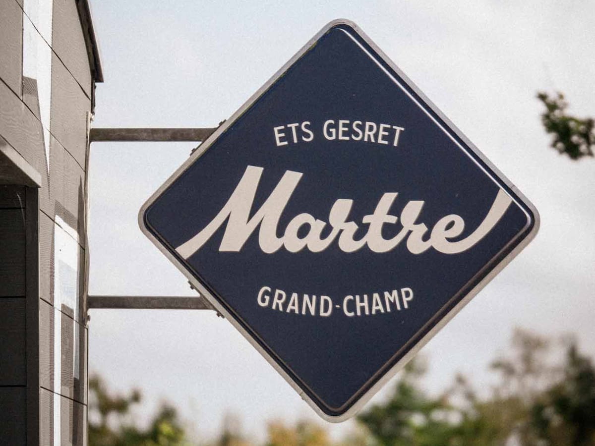 Protruding sign in white out of blue that reads "Ets Gesret, Martre, Grand-Champ".