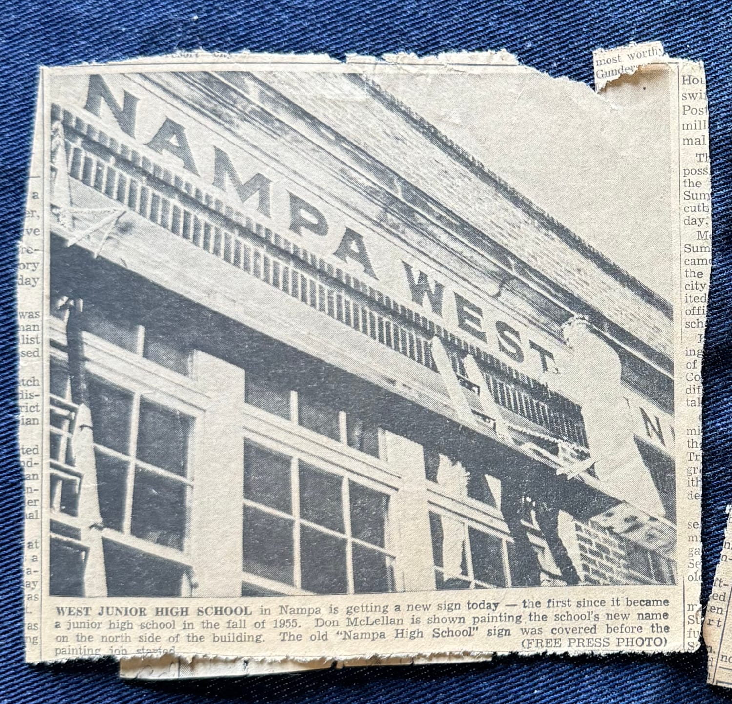 Newspaper clipping with a photo of a man on a raised platform painting a sign.