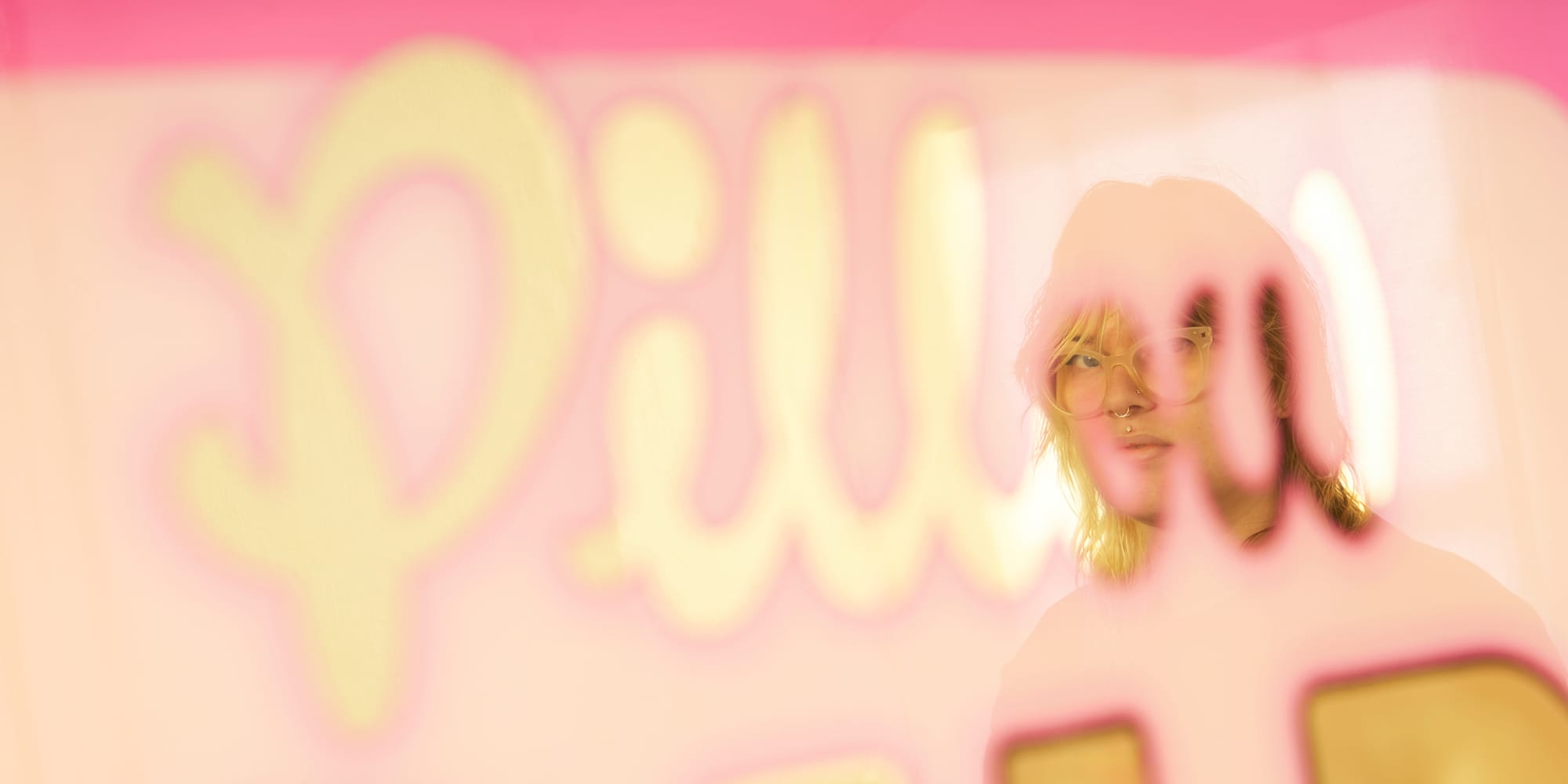 Depth of field photo with out-of-focus piece of glass gilding and the word 'pillow' visible, with a person wearing glasses reflected and in focu in the letters 'o' and 'w'.